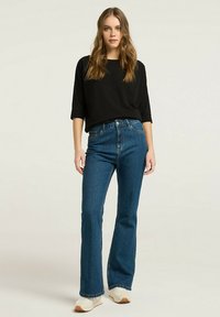 Czarny krótkosłowy top w połączeniu z niebieskimi jeansami o wysokim stanie i białymi trampkami, z klasycznym wykończeniem denimu i minimalistycznym wzornictwem.