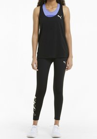 Débardeur noir associé à un legging noir avec des accents blancs et dorés. Le mannequin porte des baskets blanches, mises en valeur par un sous-t-shirt violet.