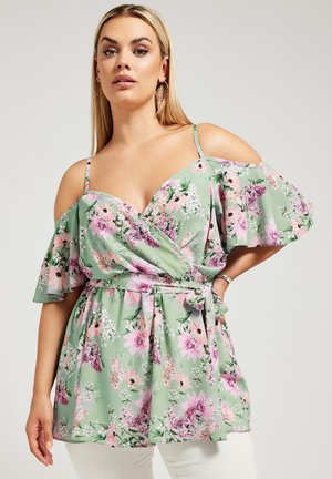 Top floreale avvolgente verde con fiori rosa e bianchi, maniche scoperte, dettagli arricciati e un particolare in vita legato.