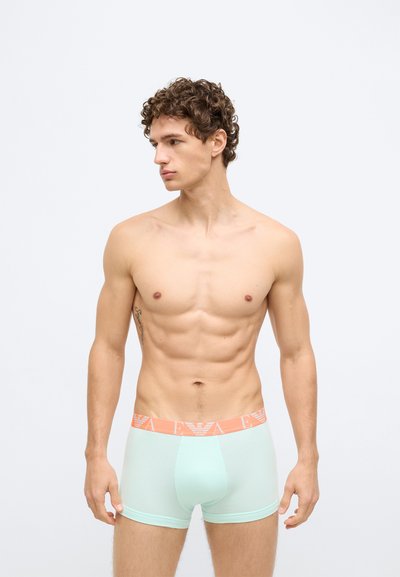 Boxers masculinos de verde menta com cós laranja contrastante com detalhes em relevo do logótipo. O tecido parece liso e elástico.