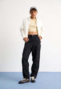 Modelo vistiendo una chaqueta corta blanca, un top ceñido beige, pantalones cargo negros con bolsillos frontales y zapatillas marrones con acentos verdes.