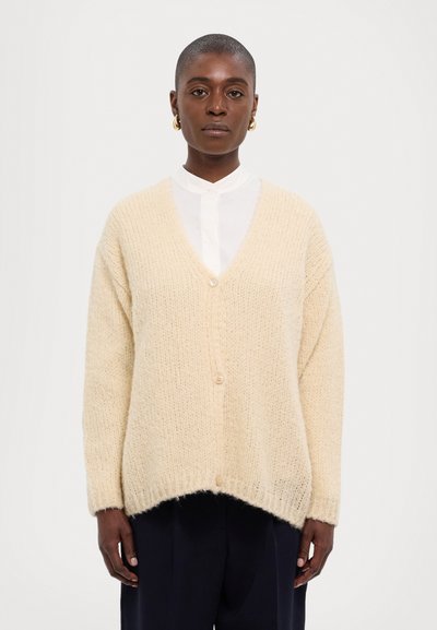 Helle beige Strickjacke mit V-Auschnitt, langen Ärmeln und Knopfverschluss. Weiche Textur und eine leicht übergroße Passform mit abgerundetem Saum.