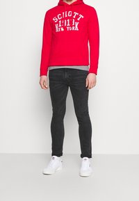 Felpa rossa con scritte bianche, maglia grigia a strati sotto, jeans skinny neri e sneakers bianche con dettagli rossi. Tessuto dalla texture liscia.