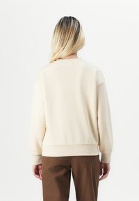 Hanorac bej cu gât rotund, manșete și tiv cu nervuri. Fabricat dintr-un material moale; are un croi lejer și un design minimalistic.