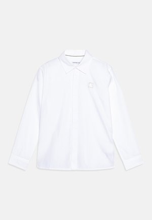Camicia bianca a maniche lunghe in cotone con colletto classico, dotata di una piccola etichetta con il logo Calvin Klein sul petto.
