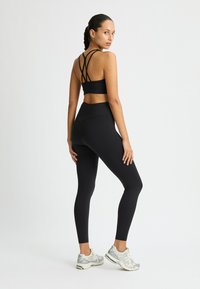 Reggiseno sportivo nero con design a incrocio sulla schiena e leggings a vita alta, abbinati a scarpe da atletica grigie. Tessuto morbido e elastico.