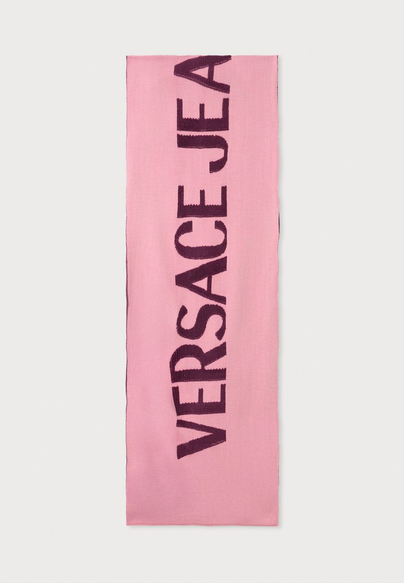 Vaaleanpunainen kankainen huivi, jossa on rohkea tummanvioletti "VERSACE JEAN" -teksti. Sileä pinta, siistit reunat, suorakaiteen muotoinen ja ilman ylimääräisiä koristeita.