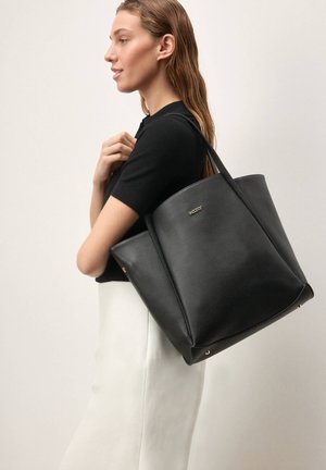 Sac fourre-tout en cuir noir au design structuré, doté d'accents en métal doré. Finition texturée et deux longues anses pour un transport facile.