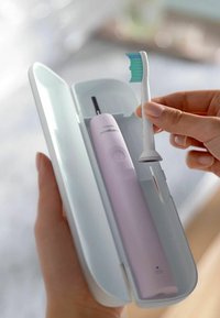 Elektrische tandenborstel in witte behuizing; roze lichaam met aan-uitknop; inclusief een tandenborstelkop met blauwe en witte haren.