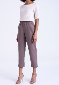 Beżowa bluzka z krótkim rękawem w zestawieniu z szarymi spodniami z elastycznym pasem, sięgającymi kostek. Modelka nosi sandały na wysokim obcasie z paskami.