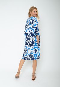 Niebieska i biała sukienka w wzory z rękawami ¾, kieszeniami i luźnym krojem, z kwiatowym i paisleyowym wzorem na granatowym tle.