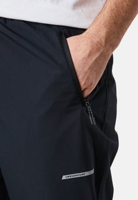 Schwarze Sporthosen mit einer Reißverschlusstasche, glatter Textur und einem silbernen Logo an der Seite. Entworfen für Funktionalität und Komfort.