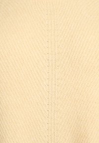 Tessuto lavorato a maglia color beige chiaro con un motivo a coste diagonali e strutturato. Il materiale appare morbido e leggermente elastico.