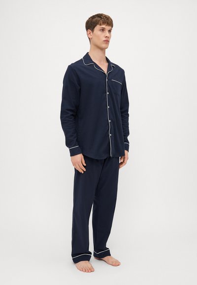 Conjunto de pijama em algodão azul-marinho, composto por uma camisa com botões, com acabamentos brancos e um bolso no peito, combinado com calças de cintura elástica a condizer.