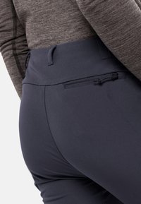 Pantaloni stretch navy con un design aderente, vita elasticizzata e una tasca con zip sicura sulla schiena, abbinati a un top grigio a manica lunga.