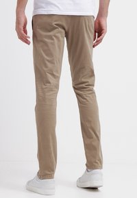 Beiga byxor med smal passform i mjukt tyg, med en slät yta och minimalistisk design. Bärs med vita sneakers.