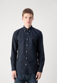 Marineblauwe overhemdd met een puntkraag, voorzien van witte knopen en een subtiele rode "BOSS" logo op de borst. Een gladde textuur van de stof.