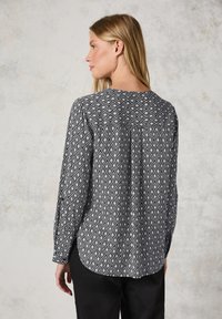 Svartvit mönstrad skjorta med diamantdesign, lång ärm och rundad halsringning. Baksidan har veckdetaljer och en avslappnad passform.