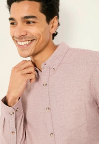 Helle rosa Button-Down-Bluse mit einem kleinen Karomuster, Kragen und einer einzelnen Brusttasche. Knöpfe haben einen kontrastierenden Farbton. Strukturierter Stoff.