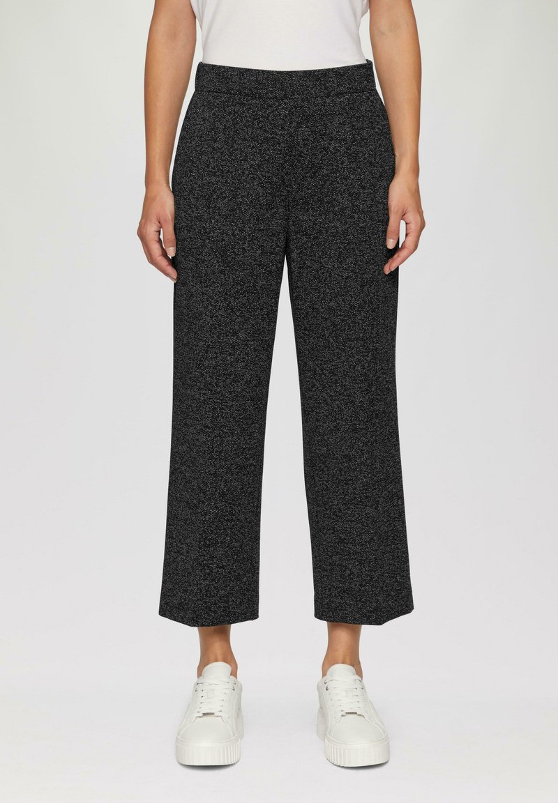Un pantalon large noir texturé avec une taille élastique, présentant un motif chiné subtil, associé à des baskets blanches.