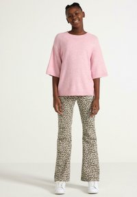 Lyserød strikket sweater med brede ærmer, parret med flagrende leopardmønstret bukser i jordtoner og hvide sneakers. Glat tekstur overalt.