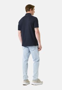 Polo shirt marine en tissu texturé, à manches courtes et avec un col contrastant, associé à un jean bleu clair et des baskets neutres.