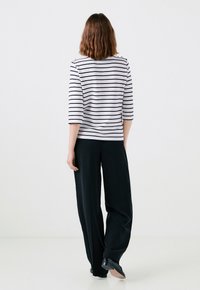 Top a righe manica 3/4 in bianco e blu navy, abbinato a pantaloni neri larghi. Il top presenta un colletto rotondo e una silhouette aderente.