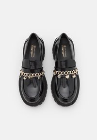 Mocassins en cuir verni noir avec une semelle épaisse, ornés d'une chaîne dorée avec des breloques et d'une finition lisse.