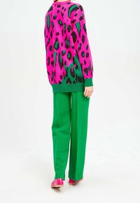 Różowo-zielony sweter w panterkę, luźny krój; zestawiony z jasnoniebieskimi spodniami i różowymi butami, gładka faktura, casualowy design.