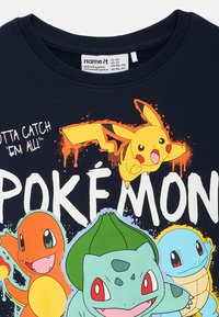 Marineblauwe T-shirt van katoen met kleurrijke Pokémon-afbeeldingen: Pikachu, Charmander, Bulbasaur en Squirtle, vergezeld van vetgedrukte tekst.