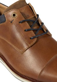 Chaussure en cuir marron au fini lisse, dotée de lacets bleu marine, d'un col en tissu marron texturé et d'une semelle blanche contrastante.