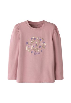 Chemise rose à manches longues avec épaules bouffantes, décorée de fleurs en forme de cœur violettes et blanches et le mot "love" en texte pailleté violet.