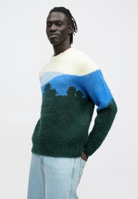 Adīts džemperis zaļā, zilā un krēmkrāsā ar ainavas dizainu. Apaļš kakla izgriezums, mīksta tekstūra un brīvs piegriezums.