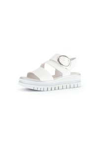 White sandal with cross straps, circular silver accent, thick white sole, and textured tread. Smooth material, open design for breathability.
