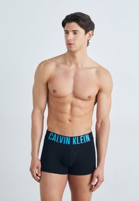 Sorte boxershorts med en blå "CALVIN KLEIN" logo linning. Stoffet fremstår glatt og elastisk, og passer tett til kroppen.