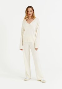 Crème gebreide trui met een V-hals en lange mouwen, gecombineerd met bijpassende losse broek. Soepele textuur, subtiele ribbelstructuur.