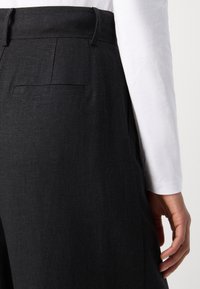 Mustat pellavahousut, joissa on tasainen etuosa, sivutaskut ja yksi takatasku. Kankaassa on hienovarainen tekstuuri.