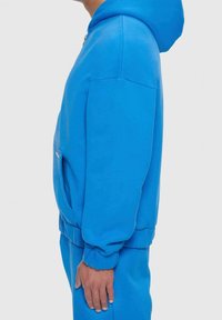 Blaues Kapuzenpullover mit Frontreißverschluss, großer Kapuze und Seitentaschen. Glatte Textur, gerippte Bündchen und Saum, entworfen für eine lässige Passform.