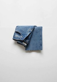 Gefaltete blaue Jeans aus Denim vor einem schlichten weißen Hintergrund, sichtbare Nähte und ein kleines weißes Etikett.