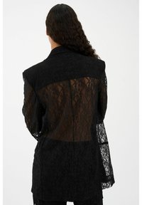 Melnas mežģīņu žaketes ar caurspīdīgu aizmuguri, ar strukturētu apkakli un garām piedurknēm. Visā virsmā ir teksturēts ziedu raksts.