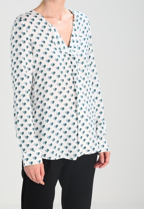 Long-sleeve blouse in lightweight, sheer fabric featuring a white background with teal heart patterns and a V-neck design.