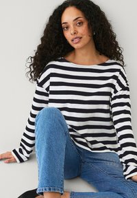 Zwart-witte gestreepte lange mouwen shirt met een brede halslijn, gecombineerd met blauwe denim. Heeft een relaxte pasvorm en een zachte katoen stof.
