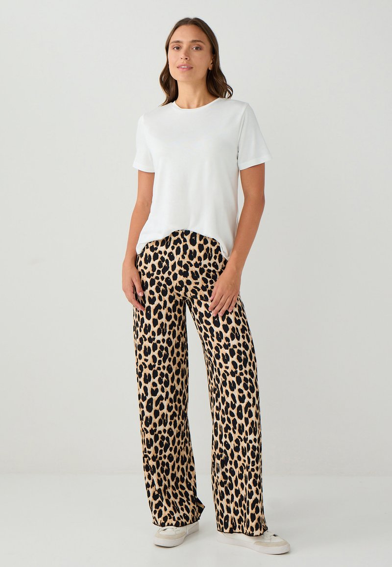 Witte t-shirt met korte mouwen, gecombineerd met bruine leopardprint wijde broek, met een zachte textuur en een relaxte pasvorm. Witte sneakers maken de look af.