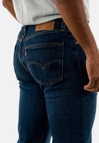 Jeans de mezclilla azul oscuro con un diseño ajustado. Incluye bolsillos traseros con un patrón de costura distintivo y una etiqueta de cuero marrón en la cintura.