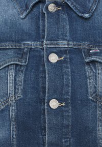 Mörkblå denimjacka med metallknappar, två bröstfickor och klassisk krage. Tyget har en subtil struktur med urtvättade områden.