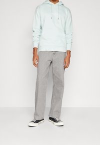 Ljusblå hoodie med dragsko och framficka, kombinerad med grå jeans med raka ben och svarta sneakers med vita sulor.