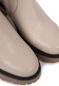 Botas de tobillo de cuero beige con puntera redonda, suela de goma negra y superficie texturizada. Presenta un tacón bajo y grueso.