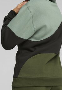 Fleece sweatshirt met een color-block ontwerp, met een lichtgroene bovenkant, zwarte middenstuk en olijfgroene onderste secties. Zachte textuur.