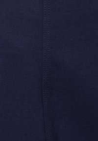 Tissu en coton bleu marine avec une texture lisse, présentant un détail de couture visible courant verticalement. Aucun motif ni accessoire présent.