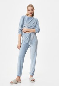 Conjunto de lounge azul claro hecho de un tejido suave y texturizado. Camiseta de manga larga con un corte holgado, acompañada de pantalones con cordón a juego. Zapatillas suaves.